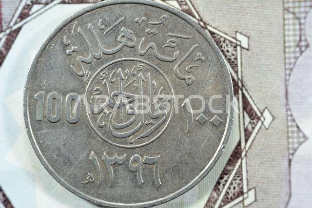 الوجه الخلفي لعملة سعودية قديمة من فئة مئة هللة، ترجمة (١٠٠ هللة = ١ ريال سعودي، سلسلة ١٣٩٦ هـ)، نقش فوق الكتابة في دائرة