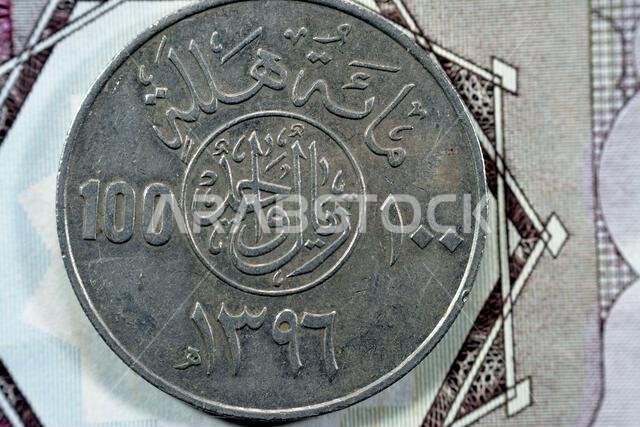 الوجه الخلفي لعملة سعودية قديمة من فئة مئة هللة، ترجمة (١٠٠ هللة = ١ ريال سعودي، سلسلة ١٣٩٦ هـ)، نقش فوق الكتابة في دائرة