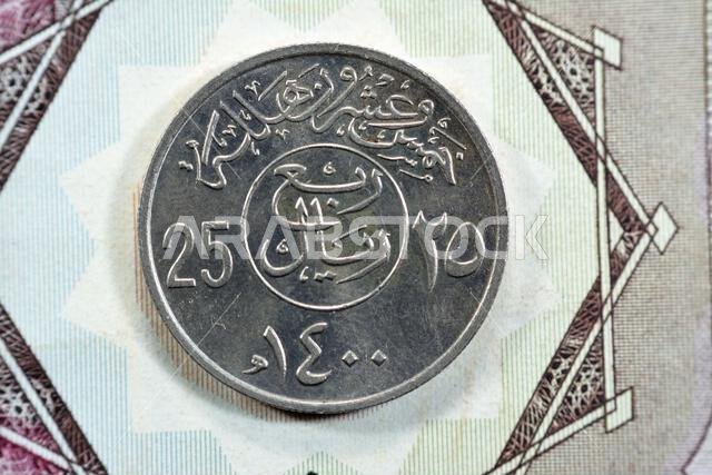الوجه الخلفي لعملة سعودية قديمة من فئة ربع ريال (25 هلالة، سلسلة 1400 هـ)، مع وجود نقش فوق الكتابة داخل دائرة.