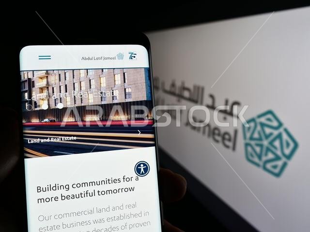 Person holding cellphone with webpage of Saudi Arabian company Abdul Latif Jameel (ALJ) on screen with logo. Focus on center of phone display.