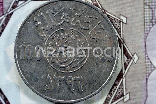 الوجه الخلفي لعملة سعودية قديمة من فئة مئة هللة، ترجمة (١٠٠ هللة = ١ ريال سعودي، سلسلة ١٣٩٦ هـ)، نقش فوق الكتابة في دائرة
