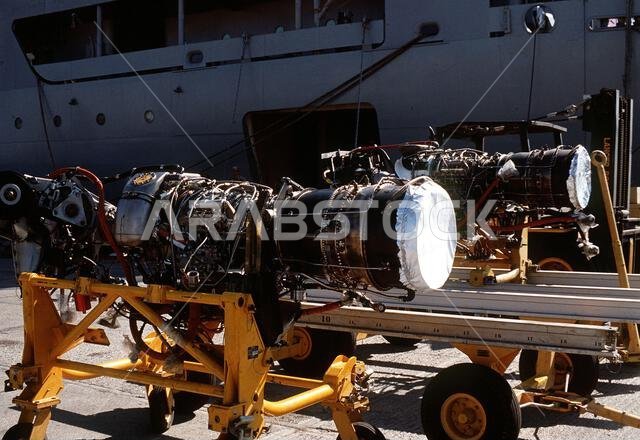 محركات نفاثة راسية على الرصيف بجانب سفينة الإمداد الجوي يو إس إن إس كورتيس (T-AVB-4) خلال عملية درع الصحراء. وحدة صيانة طيران تابعة لسلاح مشاة البحرية الأمريكية متمركزة على متن كورتيس. الموضوع: عملية/سلسلة: درع الصحراء، القاعدة: الجبيل، الدولة: المملكة العربية السعودية. محركات نفاثة راسية على الرصيف بجانب سفينة الإمداد الجوي يو إس إن إس كورتيس (T-AVB-4) خلال عملية درع الصحراء. وحدة صيانة طيران تابعة لسلاح مشاة البحرية الأمريكية متمركزة على متن كورتيس. الموضوع: عملية/سلسلة: درع الصحراء، القاعدة: الجبيل، الدولة: المملكة العربية السعودية.