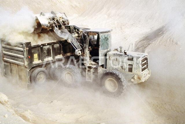 A Seabee from Naval Mobile Construction Battalion 40 (NMCB-40) empties the bucket of his front loader into the back of a dump truck while excavating a pit for an ammunition supply point during Operation Desert Shield.. Subject Operation/Series: DESERT SHIELD Country: Saudi Arabia(SAU)