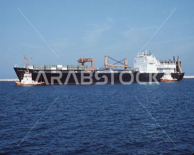 تقوم قاطرات الميناء بمناورة سفينة شحن المركبات "بي إف سي يوجين أ. أوبريجون" (T-AK-3006) باتجاه رصيف الميناء خلال عملية درع الصحراء. السفينة تابعة لسرب سفن التمركز البحري المسبق رقم 1. العملية/السلسلة: درع الصحراء. القاعدة: الجبيل. الدولة: المملكة العربية السعودية.