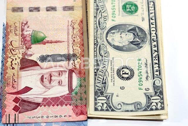 ورقة نقدية من فئة 100 ريال سعودي تحمل صورة الملك سلام والمسجد النبوي، وأخرى من فئة 20 دولاراً أمريكياً تحمل صورة الملك سلام والمسجد النبوي.