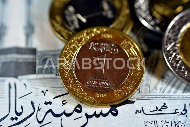 الوجه الخلفي لعملة معدنية من فئة ريال سعودي واحد (1 ريال) من سلسلة 1438 هـ 2016، معزولة مع عملات سعودية أخرى على ورقة نقدية من فئة خمسمائة ريال (500 ريال).
