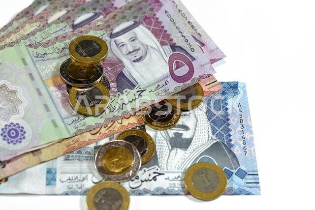 أوراق نقدية وعملات معدنية من الريال السعودي، تتضمن رزمة من فئات 500 و100 و5 ريالات، بالإضافة إلى عملات معدنية من فئتي 1 و2 ريال، تحمل صورة الملك سلمان بن عبد العزيز آل سعود.