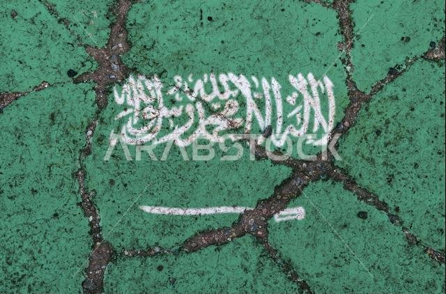 Saudi Arabia flag on cracked asphalt. The concept of crisis, default, economic collapse, pandemic, conflict, terrorism in the country. Out of focus im
