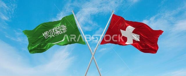 علمان متقاطعان، علم سويسرا وعلم السعودية، يرفرفان في مهب الريح تحت سماء ملبدة بالغيوم. يرمز هذا العمل الفني إلى مفهوم العلاقة والحوار والسفر بين البلدين. رسم ثلاثي الأبعاد