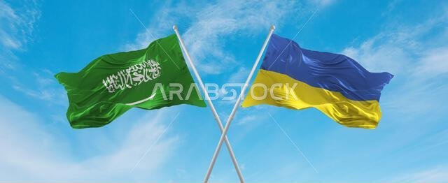 علمان متقاطعان، علم أوكرانيا وعلم السعودية، يرفرفان في مهب الريح تحت سماء ملبدة بالغيوم. يرمز هذا العمل الفني إلى مفهوم العلاقة والحوار والسفر بين البلدين. رسم ثلاثي الأبعاد.