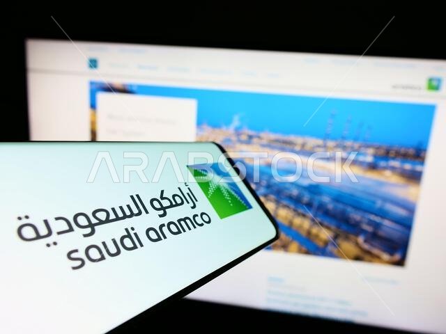 هاتف ذكي يعرض شعار شركة النفط والغاز السعودية أرامكو على شاشته أمام موقع الشركة الإلكتروني. التركيز على منتصف يمين شاشة الهاتف.