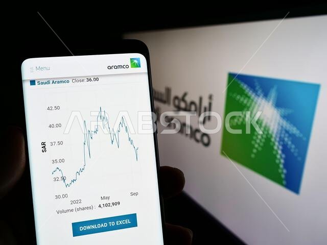 Person holding cellphone with webpage of oil and gas company Saudi Aramco on screen in front of business logo. Focus on center of phone display.