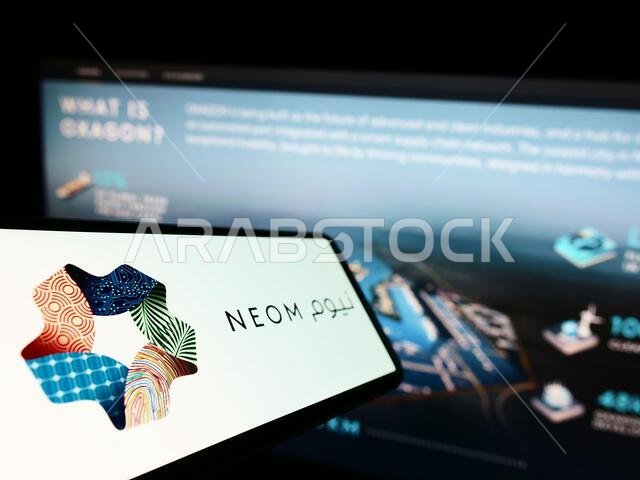 Cellphone with logo of Saudi Arabian property developer NEOM Company on screen in front of website. Focus on center-left of phone display.