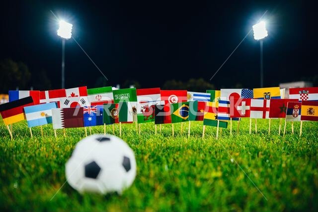Football ball on green grass. 32 flags of all nations. Dark background, Stadium in night. Artificial light. Black edit space