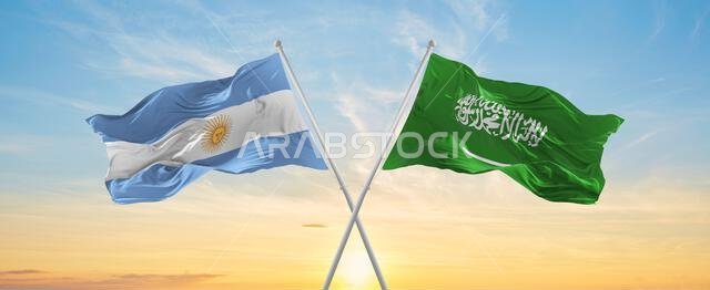 تتقاطع أعلام الأرجنتين والسعودية الوطنية وترفرف في مهب الريح تحت سماء ملبدة بالغيوم. ترمز إلى العلاقة والحوار والسفر بين دولتين.