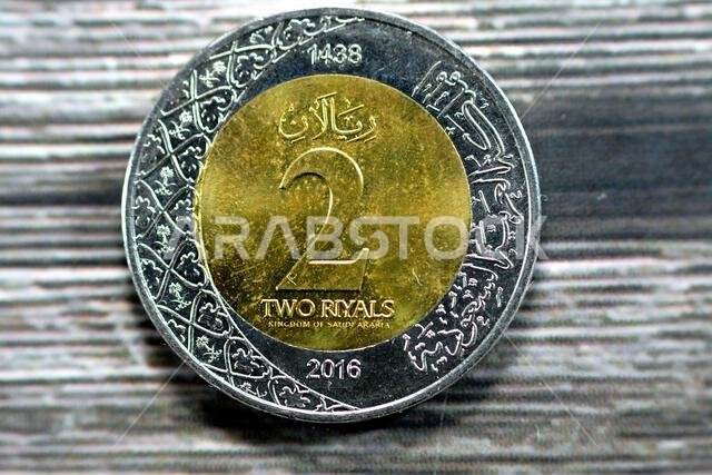 الوجه الخلفي لعملة معدنية من فئة ريالين سعوديين، إصدار عام 1438 هـ/2016م، يحمل شعارات نبالة متعددة ضمن الزخارف النباتية ونقشًا لـ الوجه الخلفي لعملة معدنية من فئة ريالين سعوديين، إصدار عام 1438 هـ/2016م، يحمل شعارات نبالة متعددة ضمن الزخارف النباتية ونقشًا لـ
