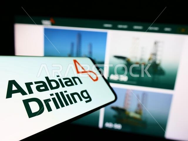 هاتف ذكي يعرض شعار شركة الحفر العربية السعودية (ADC) على شاشته أمام موقع إلكتروني. التركيز على يسار شاشة الهاتف.