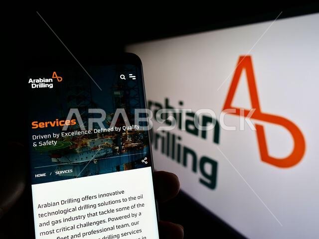 Person holding cellphone with webpage of Saudi business Arabian Drilling Company (ADC) on screen with logo. Focus on center of phone display. Person holding cellphone with webpage of Saudi business Arabian Drilling Company (ADC) on screen with logo. Focus on center of phone display.