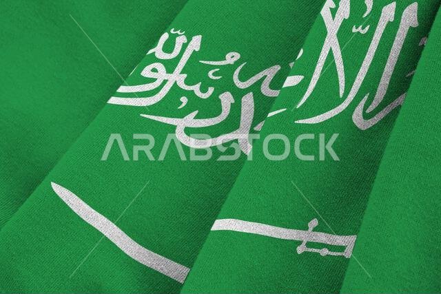 علم المملكة العربية السعودية ذو الطيات الكبيرة يرفرف عن قرب تحت إضاءة الاستوديو الداخلية. الرموز والألوان الرسمية على لافتة قماشية علم المملكة العربية السعودية ذو الطيات الكبيرة يرفرف عن قرب تحت إضاءة الاستوديو الداخلية. الرموز والألوان الرسمية على لافتة قماشية