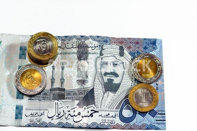 ورقة نقدية من فئة 500 ريال سعودي مع رزمة من العملات المعدنية من فئة ريال واحد وريالين، تحمل صورة الملك سلمان بن عبد العزيز آل سعود.