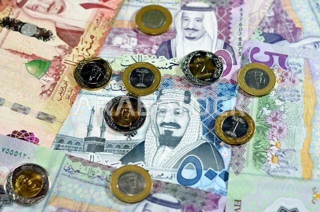 أوراق نقدية وعملات معدنية من الريال السعودي، تتضمن رزمة من فئات 500 و100 و5 ريالات، بالإضافة إلى عملات معدنية من فئتي 1 و2 ريال، تحمل صورة الملك سلمان بن عبد العزيز آل سعود.
