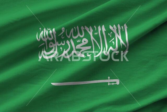 Saudi Arabia flag with big folds waving close up under the studio light indoors. The official symbols and colors in fabric banner