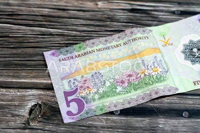 يُظهر الوجه الخلفي للورقة النقدية الجديدة المصنوعة من البوليمر فئة 5 ريالات سعودية، من سلسلة 1441 هـ 2020، حقلاً من الزهور، مع تركيز انتقائي