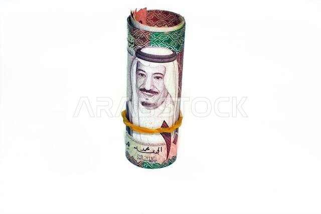 مئة ورقة نقدية من فئة مئة ريال سعودي ملفوفة بأربطة مطاطية، معزولة على خلفية بيضاء.