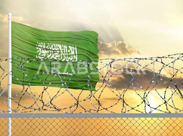 Flagpole with the flag of Saudi Arabia against the sky and behind a fence with barbed wire. The concept of protecting the borders of territories.