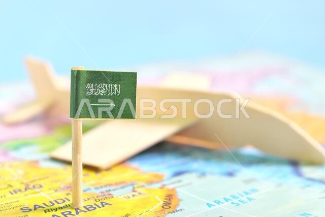 Selective focus of Saudi Arabia flag in blurry world map and airplane model. Travel and tourism destination concept.