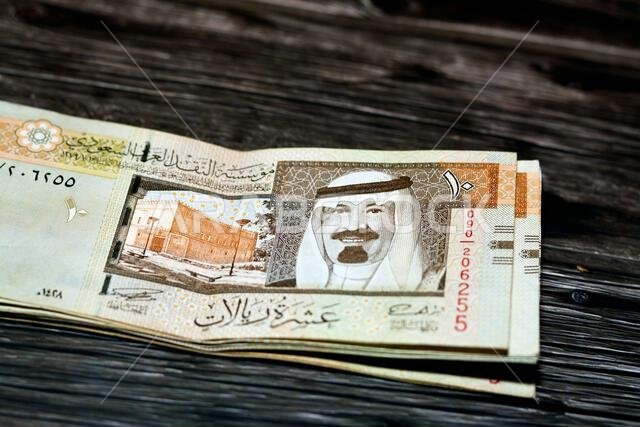 رزمة من الأوراق النقدية السعودية فئة 10 ريالات سعودية، تحمل صورة الملك عبد الله بن عبد العزيز آل سعود وقصر المربع، معزولة على