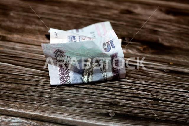 Folded Saudi Arabia money of 5 SAR five riyals isolated on wooden background, wrinkled 5 Saudi Riyals cash bill banknote, Saudi money inflation and ec