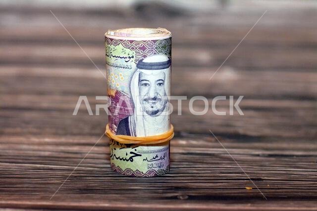 خمسة أوراق نقدية من فئة خمسة ريالات سعودية ملفوفة بأربطة مطاطية، تحمل صورة الملك سلمان ومصفاة الشيبة النفطية، المملكة العربية السعودية.