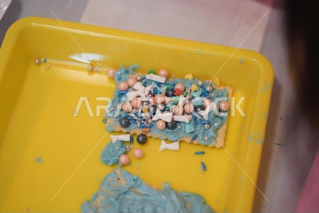 لقطة مقرّبة ليدي طفل. طفل صغير سعيد يزيّن الكعك في صينية المدرسة باللون الأزرق، ويزيّن البسكويت بسمك صغير وحبيبات سكر زرقاء. لقطة مقرّبة ليدي طفل. طفل صغير سعيد يزيّن الكعك في صينية المدرسة باللون الأزرق، ويزيّن البسكويت بسمك صغير وحبيبات سكر زرقاء.