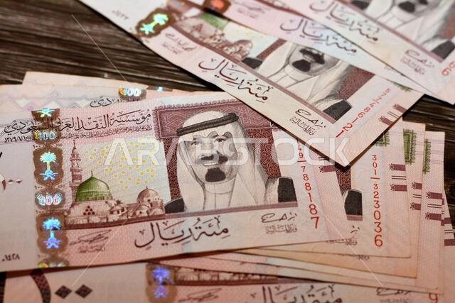 رزمة من الأوراق النقدية السعودية فئة 100 ريال سعودي، تحمل صورة الملك عبد الله بن عبد العزيز آل سعود والنبي محمد صلى الله عليه وسلم والمسجد النبوي الشريف في المدينة المنورة.