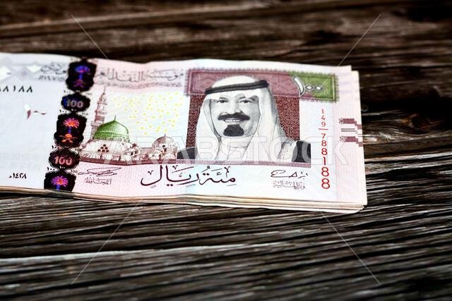 رزمة من الأوراق النقدية السعودية فئة 100 ريال سعودي، تحمل صورة الملك عبد الله بن عبد العزيز آل سعود والنبي محمد صلى الله عليه وسلم والمسجد النبوي الشريف في المدينة المنورة.