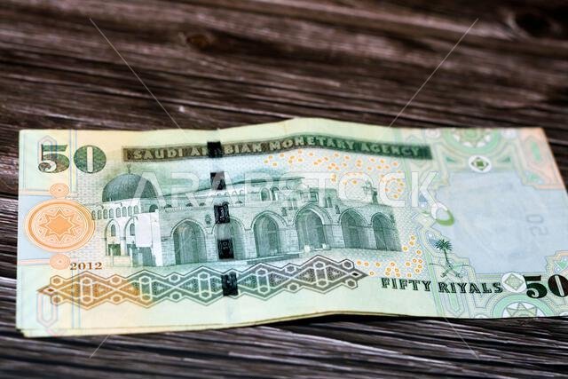مجموعة من أوراق نقدية من فئة 50 ريالًا سعوديًا، تحمل صورة المسجد الأقصى في القدس، موضوعة على ظهر ورقة نقدية، معزولة على خلفية بيضاء.