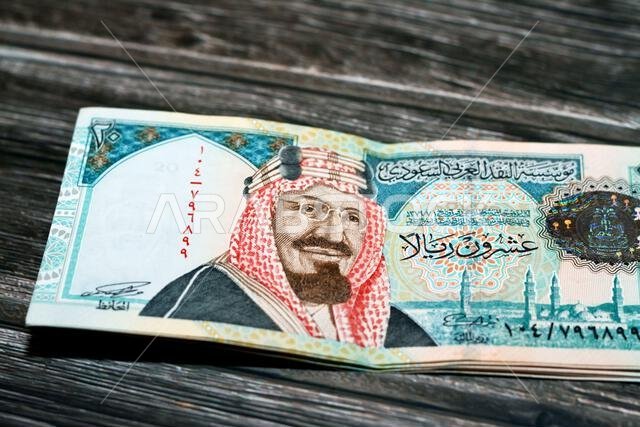 رزمة من أوراق نقدية سعودية من فئة 20 ريالاً سعودياً، تحمل صورة الملك عبد العزيز آل سعود ومسجد قباء في المدينة المنورة، معزولة على خلفية بيضاء.