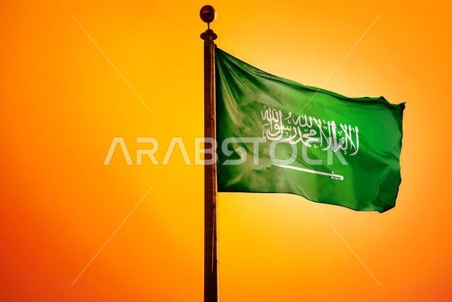 العلم الوطني للمملكة العربية السعودية على سارية علم معزول على خلفية برتقالية