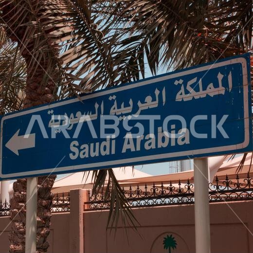 لافتة شارع زرقاء عليها سهم يشير إلى اليسار، مكتوب عليها المملكة العربية السعودية