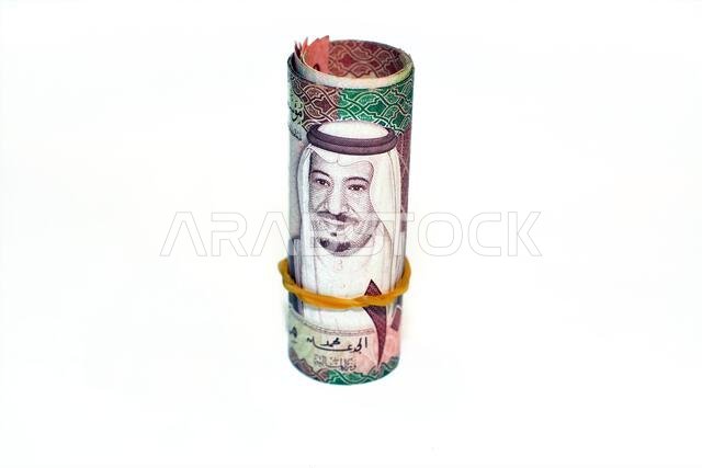 مئة ورقة نقدية من فئة مئة ريال سعودي ملفوفة بأربطة مطاطية، معزولة على خلفية بيضاء.