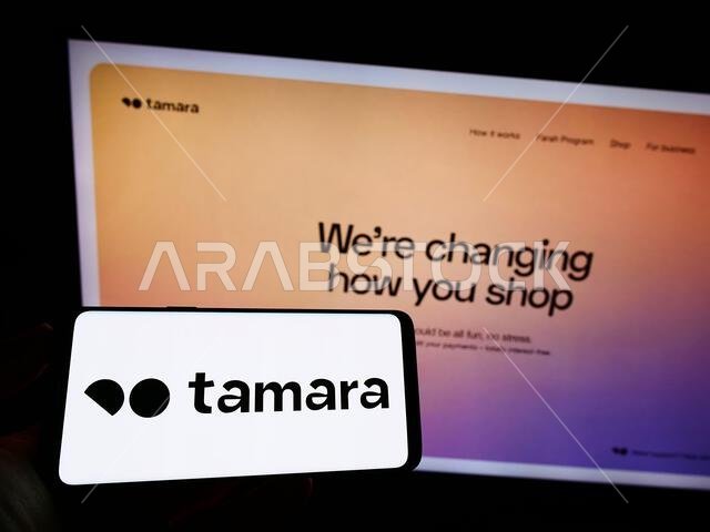 Person holding mobile phone with logo of fintech company Nakhla IT Systems LLC (Tamara) on screen in front of web page. Focus on phone display.