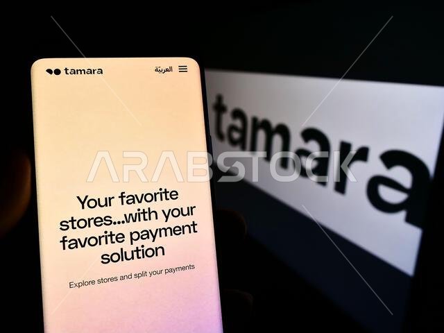 شخص يحمل هاتفًا محمولًا يعرض صفحة ويب لشركة التكنولوجيا المالية "نخلة لأنظمة تكنولوجيا المعلومات" (تامارا) مع شعارها. التركيز على منتصف شاشة الهاتف.
