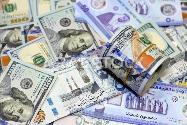 لفة نقود أمريكية عليها شريط، وكومة من أوراق الدولار الأمريكي، وأوراق نقدية أمريكية مع أوراق نقدية من الريال السعودي والإمارات الجديدة.