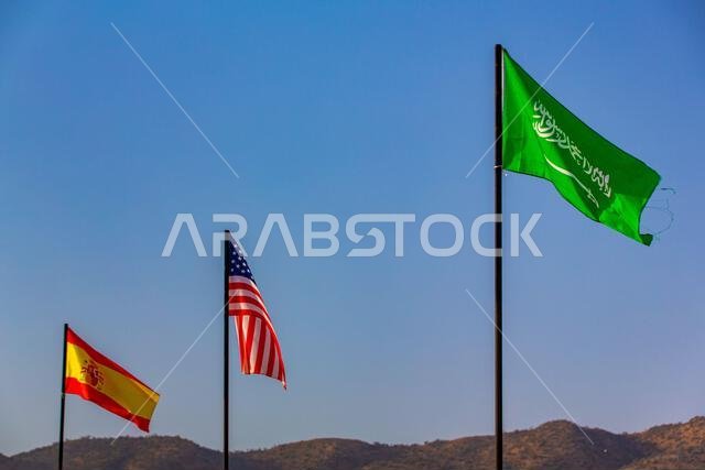 The national flag of saudi arabia, USA and spain waving in a blue sky