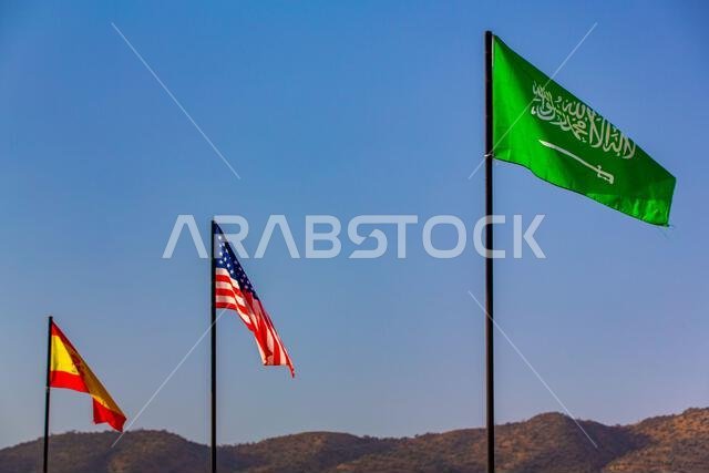 أعلام المملكة العربية السعودية والولايات المتحدة الأمريكية وإسبانيا ترفرف في سماء زرقاء