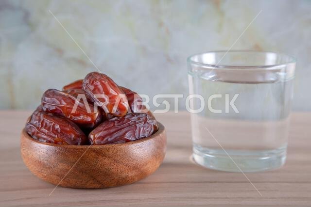 Glass of water with a bowl of date fruit on a wooden background.Muslims break the fast with water and dates Glass of water with a bowl of date fruit on a wooden background.Muslims break the fast with water and dates