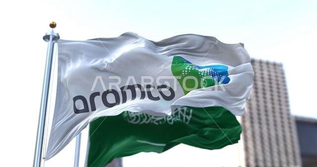 Dhahran, SA, March 2022: The flag of the Aramco oil company waving in the wind with the national flag of Saudi Arabia blurred in the background. Aramc