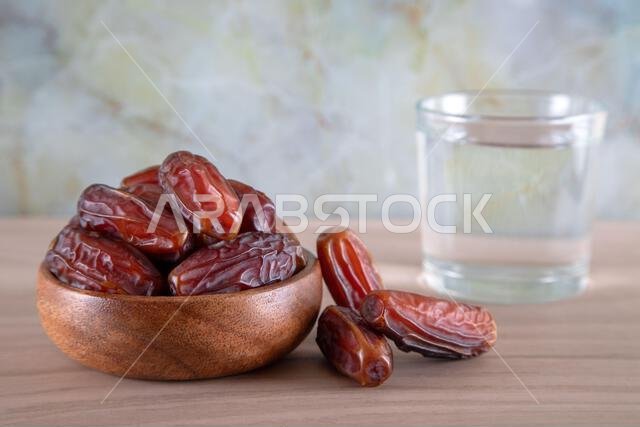 Glass of water with a bowl of date fruit on a wooden background.Muslims break the fast with water and dates Glass of water with a bowl of date fruit on a wooden background.Muslims break the fast with water and dates