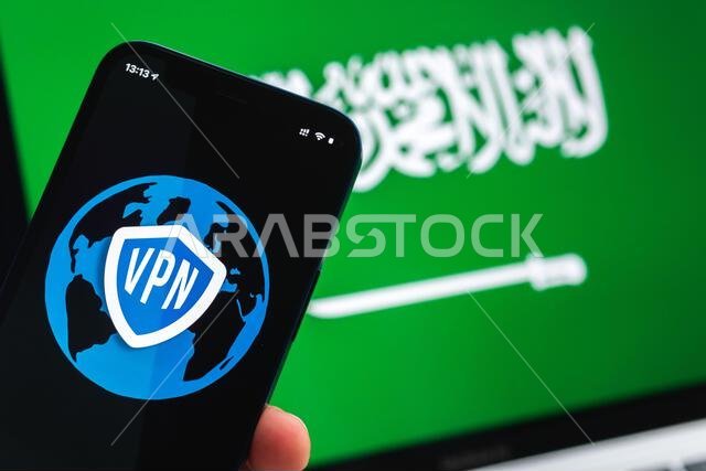 شبكة افتراضية خاصة (VPN) في السعودية. مفهوم الإنترنت الآمن والمحمي. الخصوصية. يد تحمل هاتفًا محمولًا وتطبيق VPN. علم وحاسوب محمول في خلفية الصورة.
